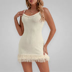 Woman wearing a cream-colored dress with fringe details on a plain background