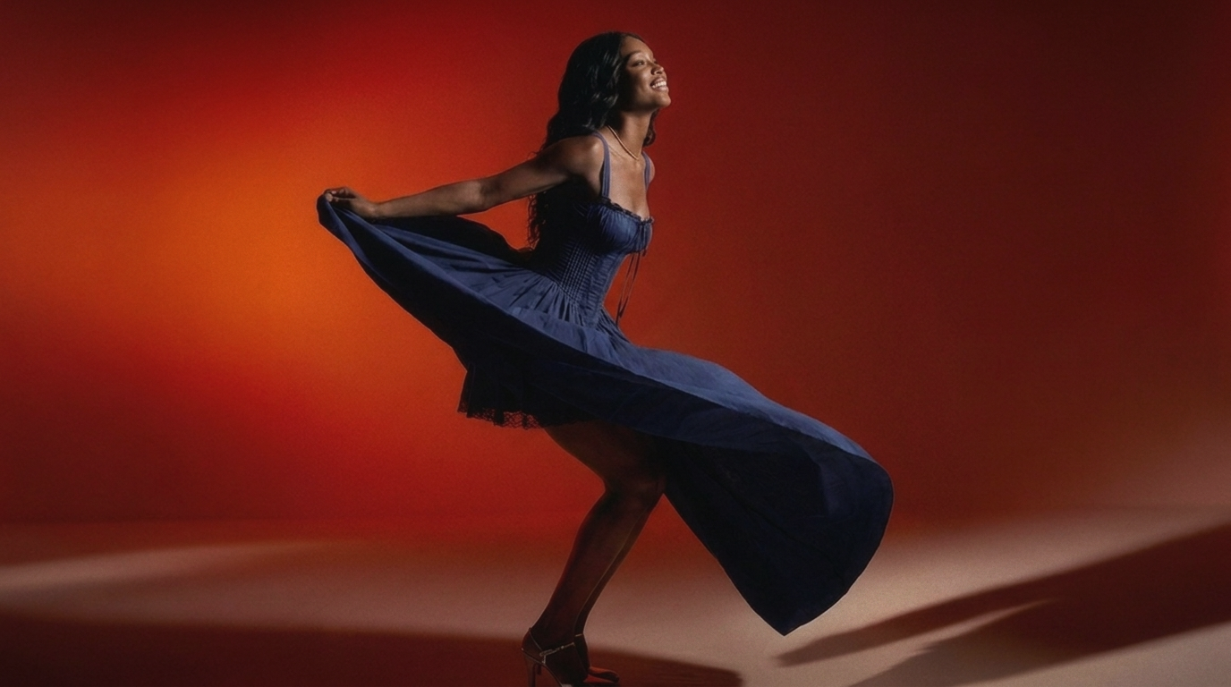 A woman in a flowing dark blue sleeveless dress twirls mid-spin against a warm orange and red gradient studio background.
